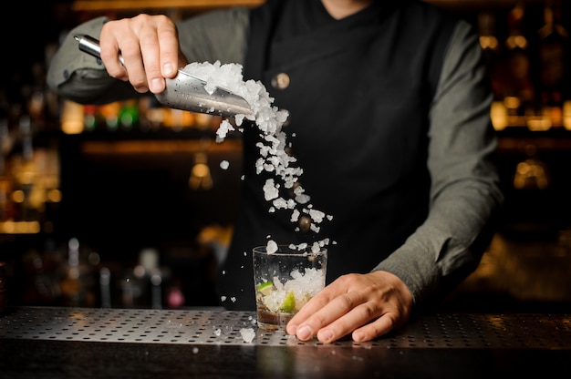 Barman vertiendo hielo en la copa de cóctel