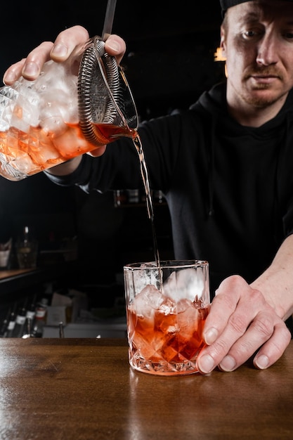 El barman vierte un cóctel Negroni tradicional mixto en el vaso del bar El barman mezcla gin campari y vermú dulce para preparar el cóctel alcohólico Negroni