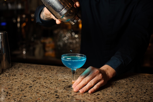 El barman vierte las últimas gotas del cóctel alcohólico Blue Lagoon de la coctelera