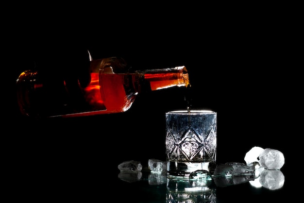 Barman vierte whisky en un vaso con hielo sobre un fondo negro, su mano sostiene una botella de ron
