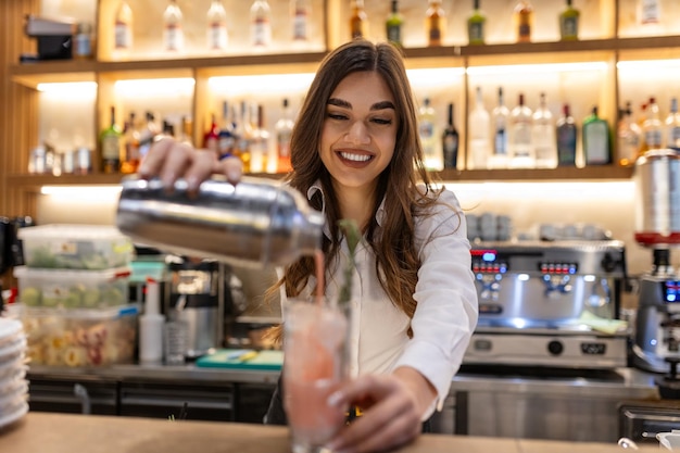 Barmanita haciendo cócteles alcohólicos en el mostrador del bar Joven barman profesional trabajando en un bar preparando cócteles