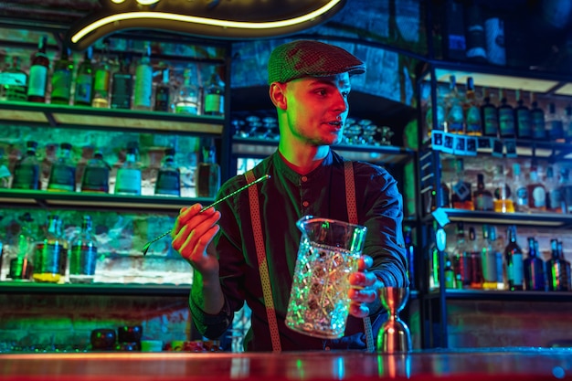 Barmann beendet die Zubereitung eines alkoholischen Cocktails mit einem Shaker in buntem Neonlicht