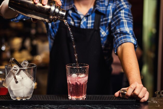 Barmann bei der Arbeit, der harten Geist in Gläser gießt und Cocktails im Detail zubereitet