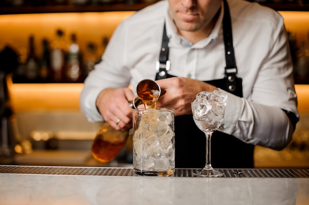 Barmann, der alkoholisches Getränk in ein Glas hinzufügt, das mit Eiswürfeln gefüllt wird