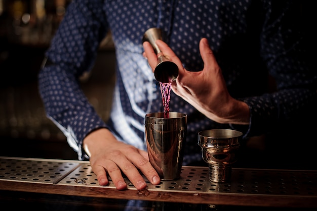 Barmannhand, die einen Teil des rosa Alkoholgetränks in den Shaker gießt