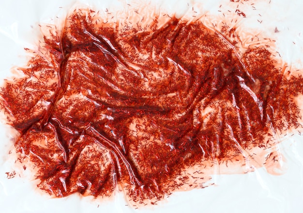 Barniz rojo derramado con destellos bajo polietileno transparente sobre un fondo blanco, una mancha