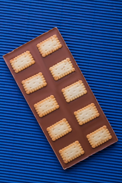 Barra de chocolate com biscoitos crocantes sobre fundo azul.