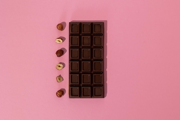 Barra de chocolate escuro com avelãs em um fundo rosa