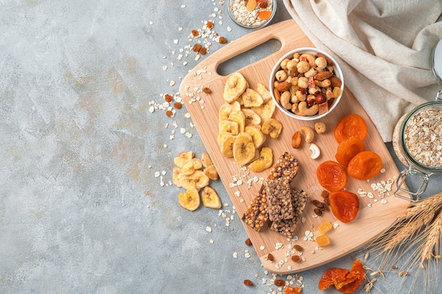 Barra de granola, nozes e frutas secas em uma tábua de madeira sobre fundo de mármore cinza claro