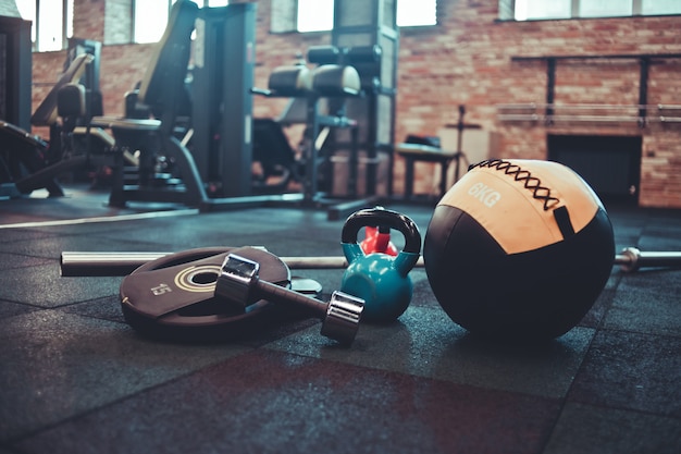 Barra desmontada, balón medicinal, pesas rusas, mancuernas acostado en el piso en el gimnasio.