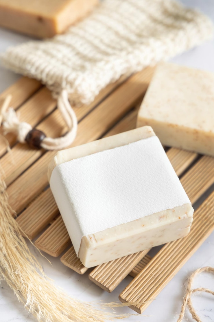Foto barra de jabón hecha a mano beige con etiqueta en blanco en una bandeja de madera cerca de la bolsa de ahorro de jabón de cerca