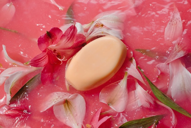 Foto barra de jabón natural en agua rosa salpicada con concepto de cuidado corporal de flores