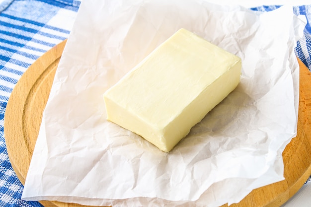 Una barra de mantequilla en una tabla de madera con un cuchillo, sobre una mesa blanca. Ingredientes para cocinar