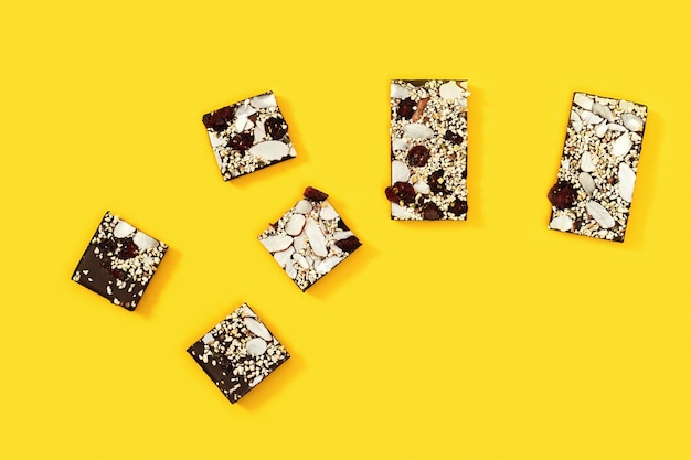 La barra mordida de chocolate se rompe en varios trozos, chocolate con nueces y frutos secos