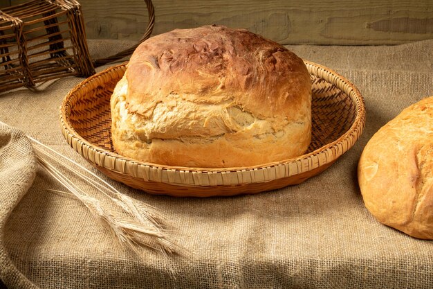 Una barra de pan blanco casero en una cesta sobre un mantel de arpillera. Cerca hay un montón de espigas de cebada.