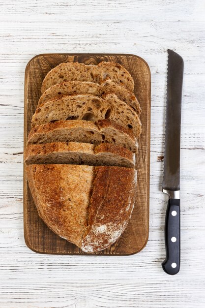 Una barra de pan fresca y un cuchillo de pan sobre una rústica mesa blanca de edad. rebanada de pan