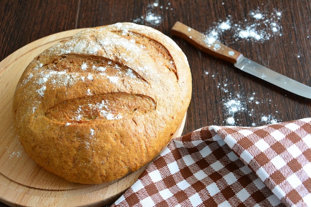 barra de pan en la tabla de cortar con cuchillo de cocina en la mesa de madera