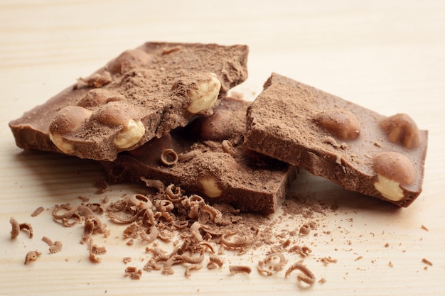 Barra quebrada de chocolate ao leite com nozes temperados com cacau em pó e moer o chocolate coloca na mesa de madeira