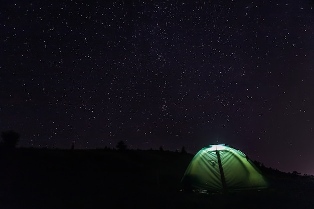 Barraca de acampamento turístico com luz dentro sob o céu estrelado