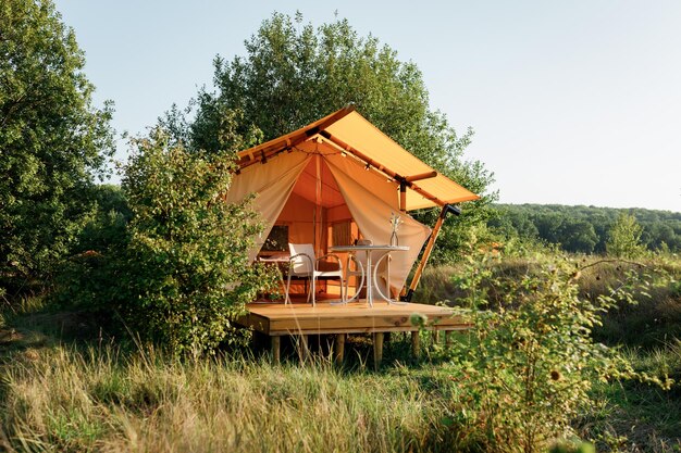 Barraca de glamping aberta e aconchegante com luz interna durante o pôr do sol Barraca de acampamento de luxo para férias de verão ao ar livre e conceito de estilo de vida de férias