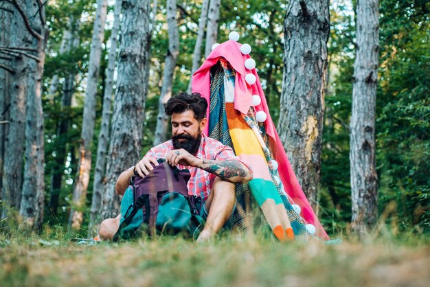 Barraca de jogo aconchegante para homem no parque florestal Caminhadas e conceito de recreação ao ar livre com viagens de acampamento planas Homem barbudo bonito se divertindo no parque de aventura