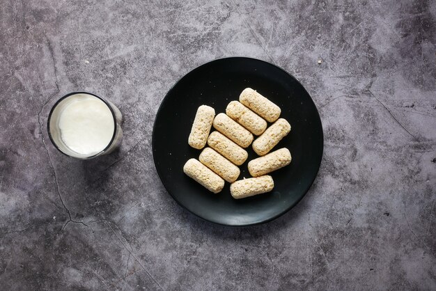 Barras de avena sabrosas en un plato y vaso de leche en la mesa