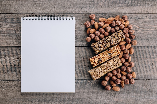 Barras da saúde, porcas misturadas e placa vazia do caderno para o texto. Barras energéticas com amêndoa e avelãs