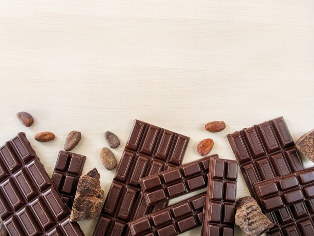 Barras de chocolate e pedaços de chocolate espalhados sobre um fundo claro