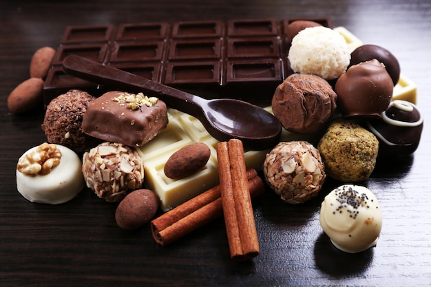 Barras de chocolates brancos e amargos com doces e colher doce no fundo liso de madeira escura