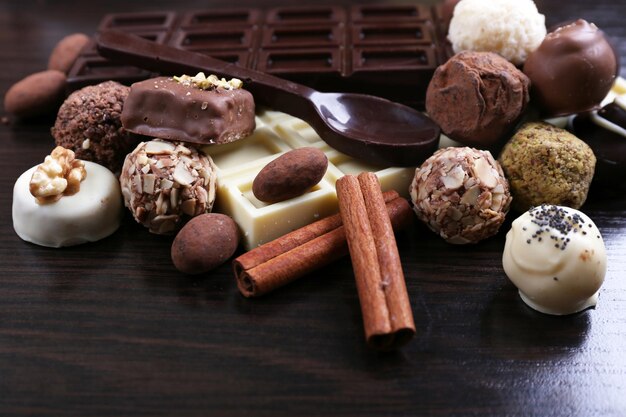 Barras de chocolates brancos e amargos com doces e colher doce no fundo liso de madeira escura