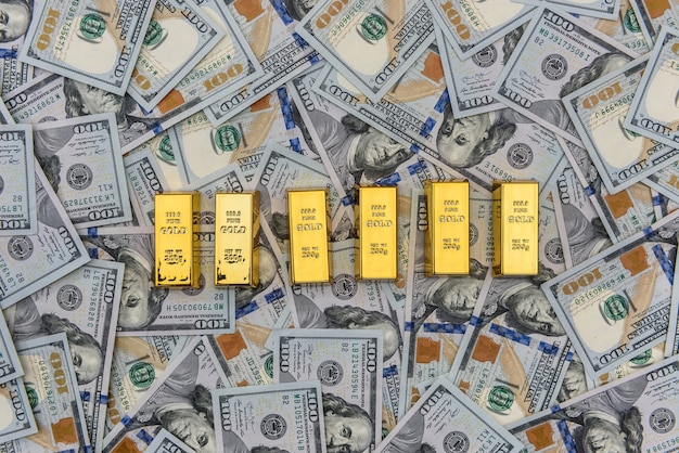 Barras de ouro com notas de cem dólares como pano de fundo