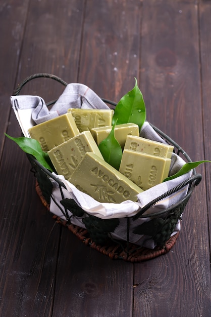 Barras de jabones verdes de aceite de oliva natural con hojas verdes en una cesta en madera oscura