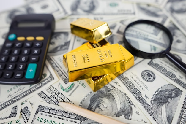 barras de oro se encuentran con una calculadora y una lupa junto a una gran cantidad de dólares concepto de ahorro financiero oro y dólares