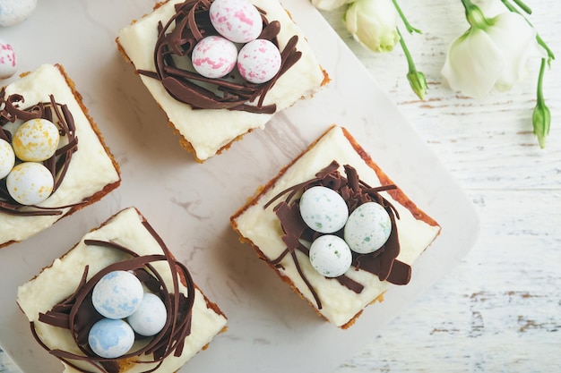 Barras de pastel de zanahorias de Pascua decoradas con nido de chocolate y huevos de caramelo de chocolate con flores de cereza o manzana en fondos de madera rústica ligera Comida tradicional de Pascua