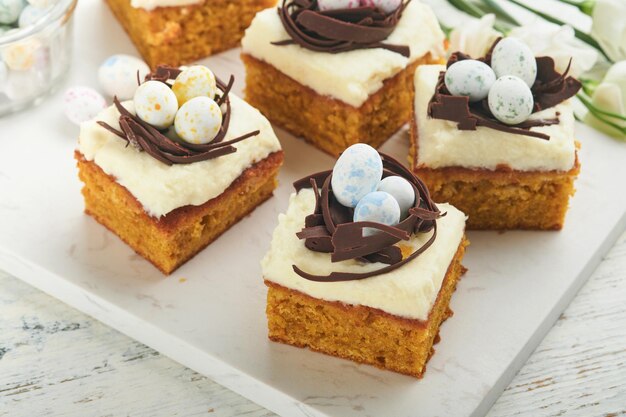 Barras de pastel de zanahorias de Pascua decoradas con nido de chocolate y huevos de caramelo de chocolate con flores de cereza o manzana en fondos de madera rústica ligera Comida tradicional de Pascua