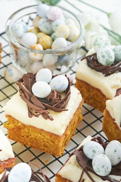 Barras de pastel de zanahorias de Pascua decoradas con nido de chocolate y huevos de caramelo de chocolate con flores de cereza o manzana en fondos rústicos de madera ligera Comida tradicional de Pascua