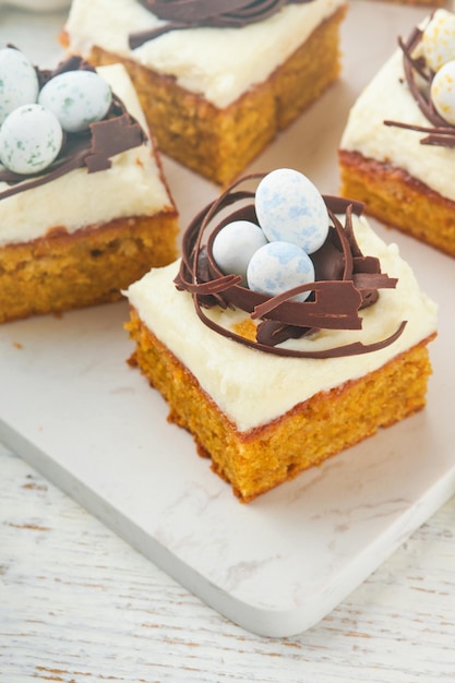 Barras de pastel de zanahorias de Pascua decoradas con nido de chocolate y huevos de caramelo de chocolate con flores de cerezas o manzanas en fondos rústicos de madera ligera Comida tradicional de Pascua