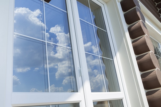 Barras de plástico de ventana blanca con el reflejo del cielo nublado azul