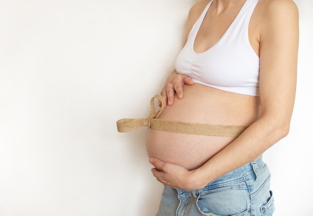 Barriga de grávida com fita de linho de lona ecológica ao redor da barriga em uma parede branca. Vista de perfil. Lugar para texto