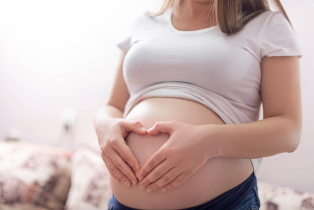 Foto barriga de grávida e braços em forma de coração na barriga em camiseta branca