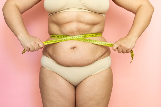 Barriga de mulher com excesso de peso cortada após o nascimento medindo sua cintura por fita Abdômen gordo cedendo dobras em excesso