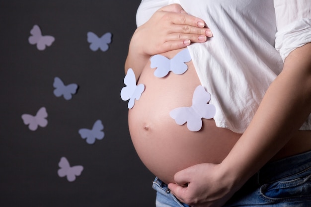 Barriga de mulher grávida com borboletas coloridas sobre fundo cinza