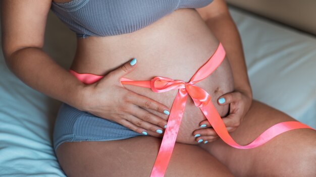 Barriga de uma grávida com uma fita rosa em volta do abdômen. close de barriga grávida