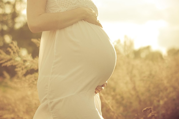 Foto barriga de uma mulher grávida fechada nos raios do sol poente