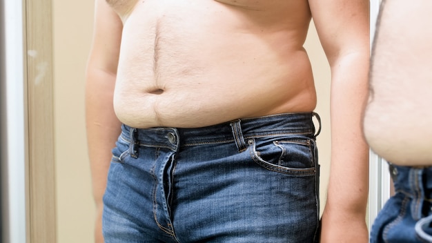 Barriga masculina gorda pendurada sobre jeans pequenos. Conceito de excesso de peso masculino, perda de peso e dieta.