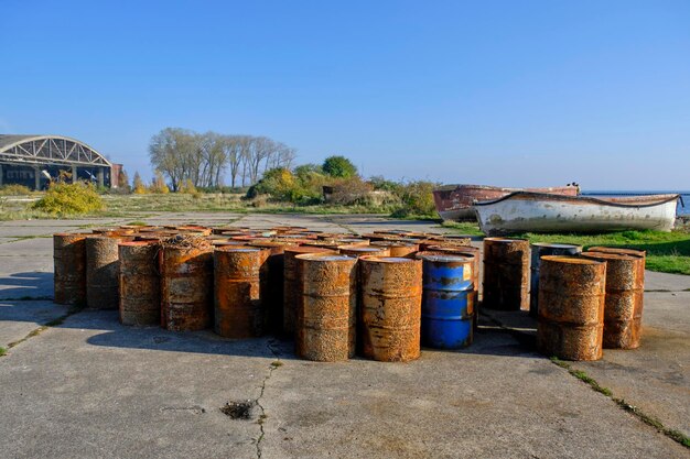 Barriles de combustible oxidado orilla contra fondo antiguo hangar y barcos