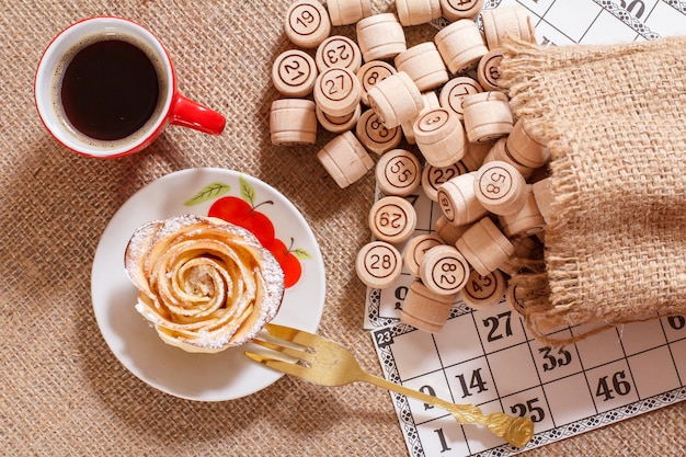 Barris de loteria de madeira em bolsa e cartas de jogo para um jogo de loteria com xícara de café e biscoito caseiro em forma de rosa sobre pires branco. vista do topo