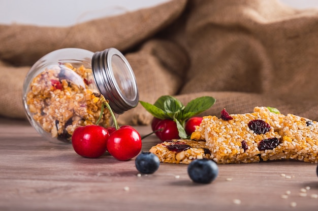 Barritas de cereales con frutos rojos, miel y sésamo para una dieta sana - Barritas de granola vegetariana casera con cerezas, semillas y miel sobre un fondo rústico.