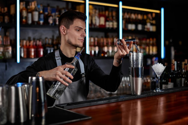 Bartender in Schürze fügt Zutaten zum Shaker hinzu