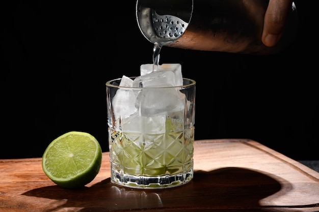 Foto bartender039s mano vertiendo una bebida en un vaso con limón y hielo para una bebida sobre un fondo negro